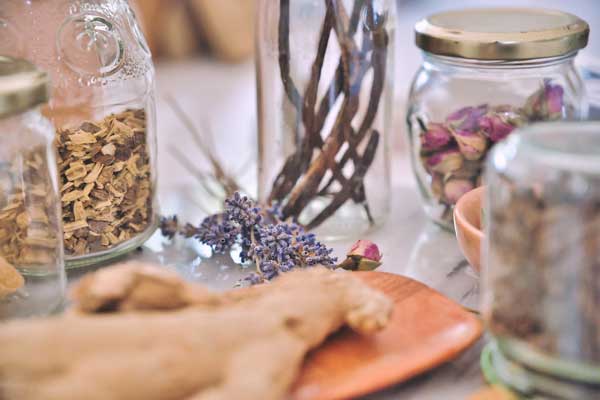 Glass jars of dried herbs arranged with lavender and botanical ingredients.
