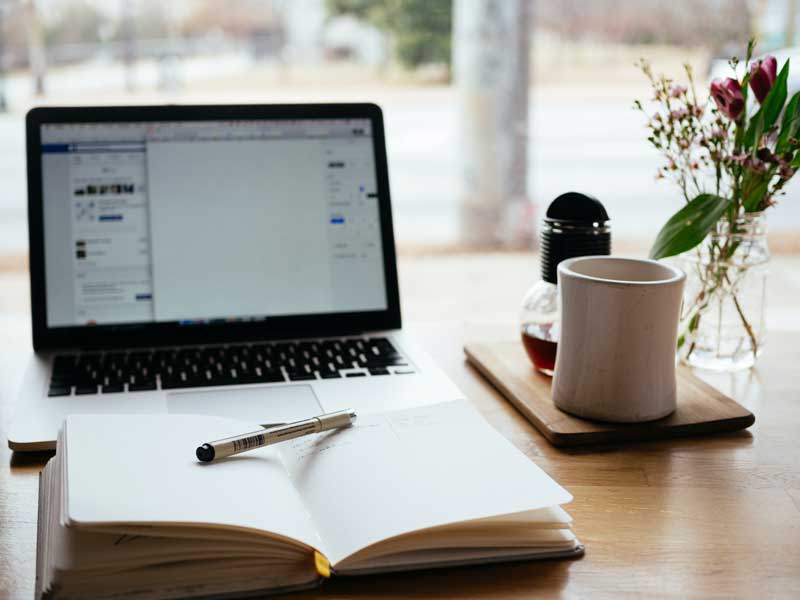 A laptop, open notebook, pen, and tea arranged for learning from home.
