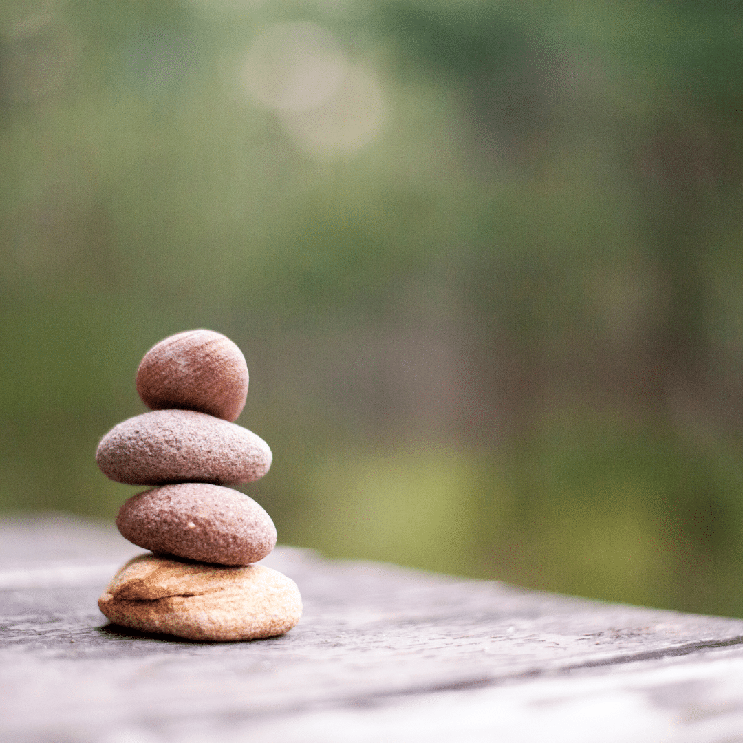 Four smooth stones stacked on a wooden surface against a softly blurred green background.